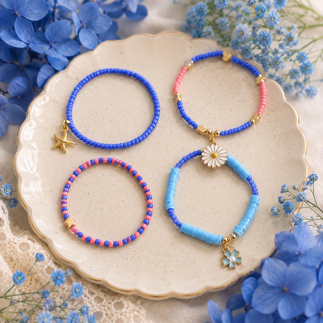 Four beaded stretch bracelets. The bracelets feature blue, pink, and light blue beads with 3 gold-tone charms including a star, blue flower and a daisy.